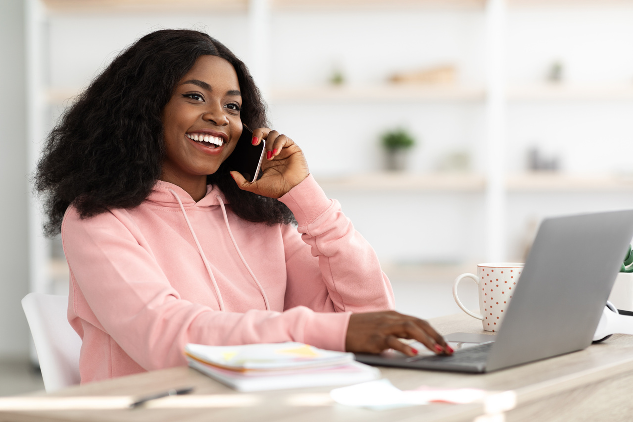 Pretty Black Lady Having Phone Conversation While Working on Laptop